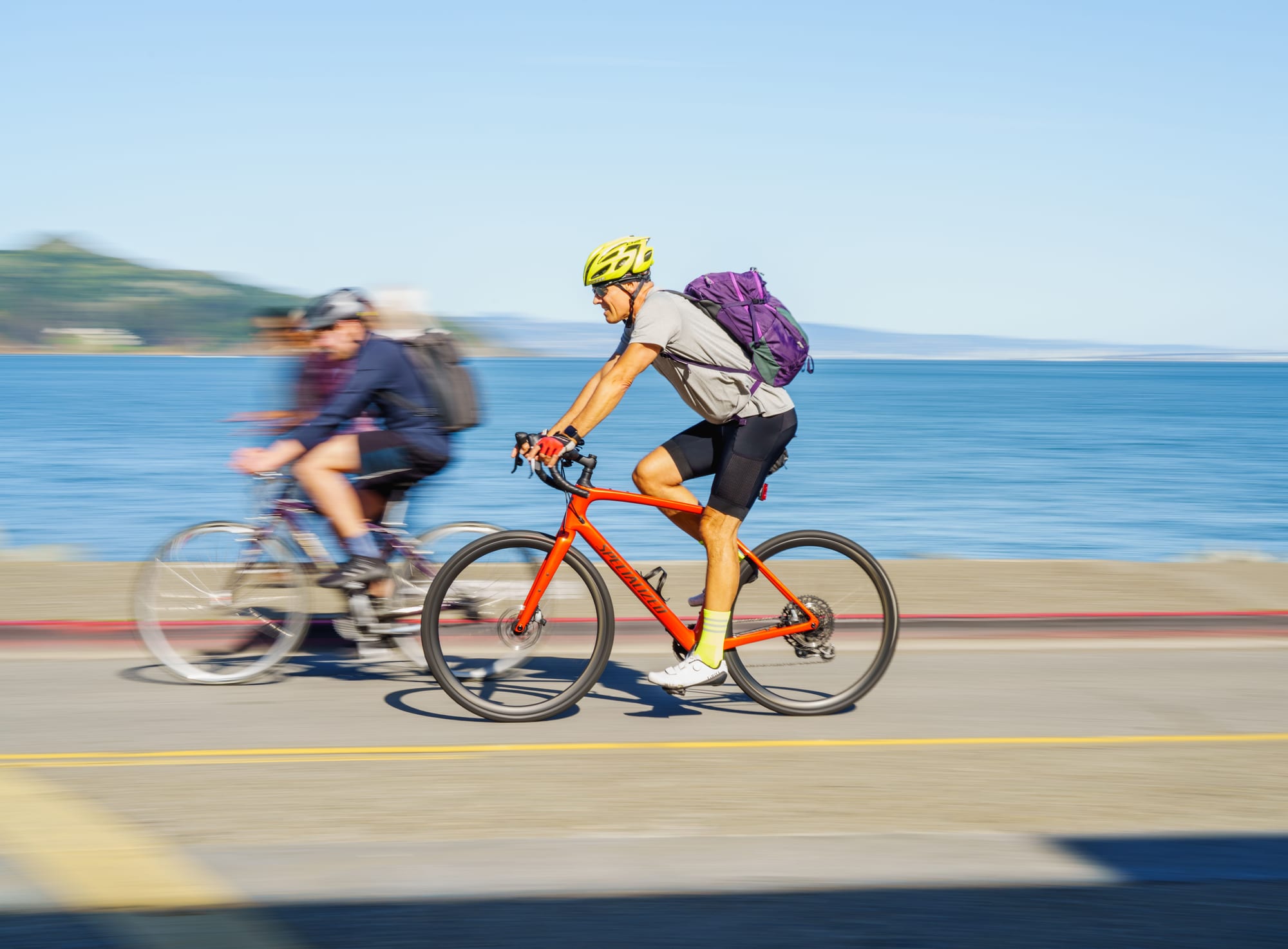 Two cyclists riding along a sunny coastal road beside the sea, similar to the IRONMAN 70.3 Phú Quốc bike leg