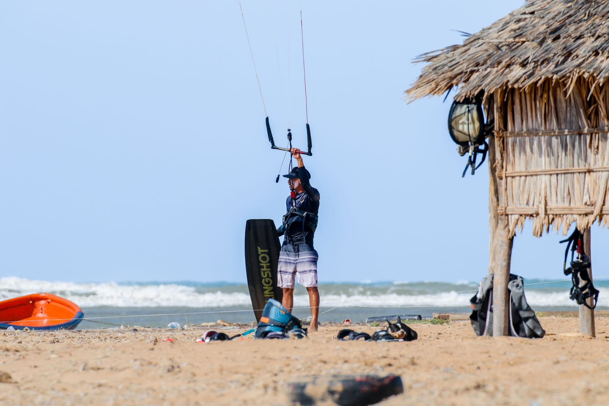 Kite gear laid out on the sand beside a thatched beach hut, ready to rig before a session
