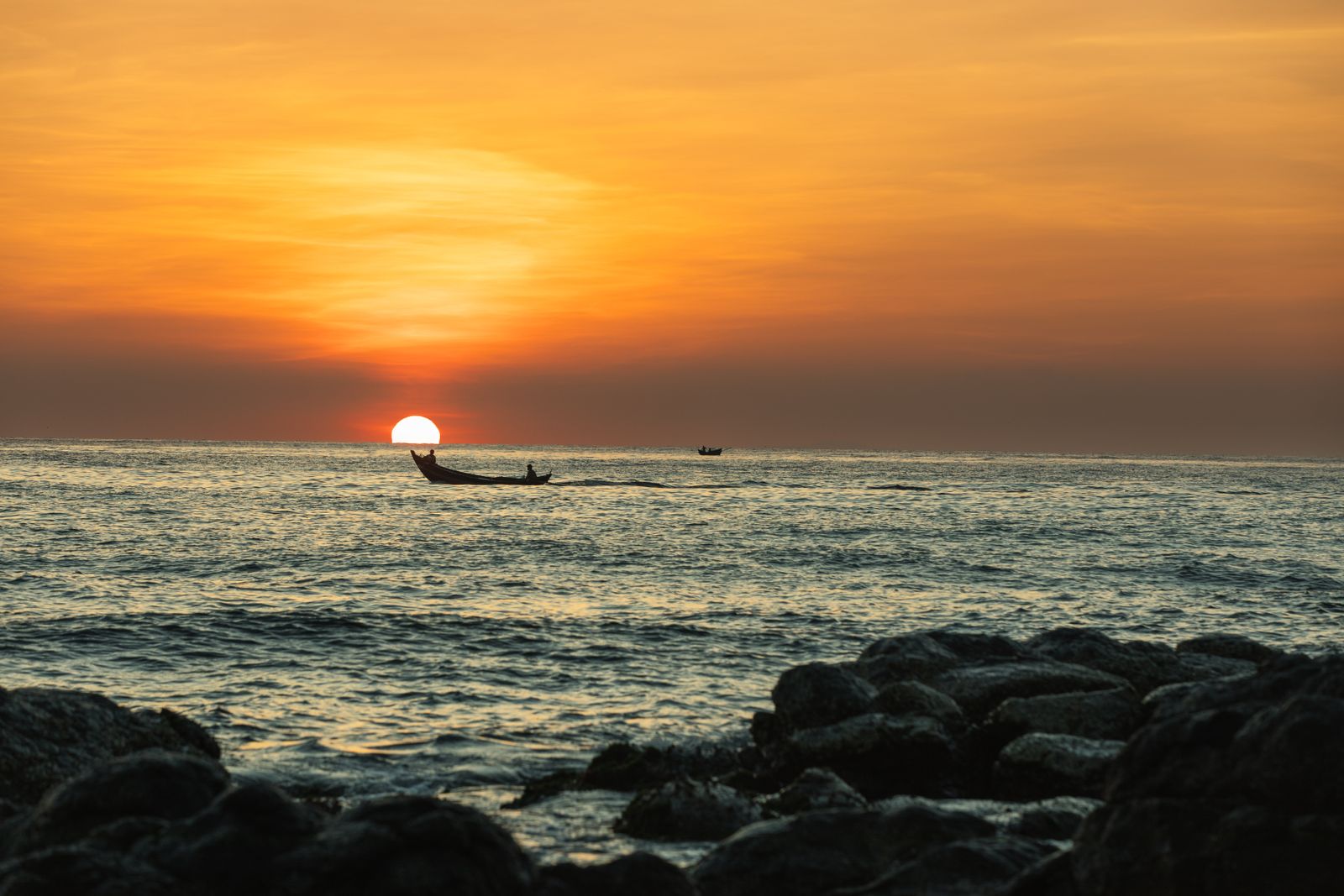 Fishing boats silhouetted against an orange sunset over the sea in Phú Quốc
