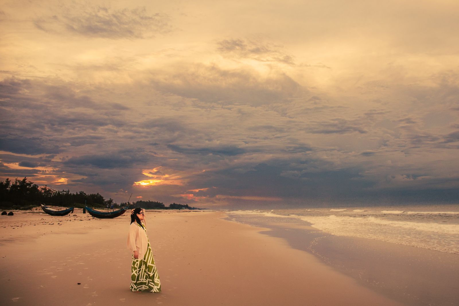A person standing alone on the beach watching the Phú Quốc sunset over calm water